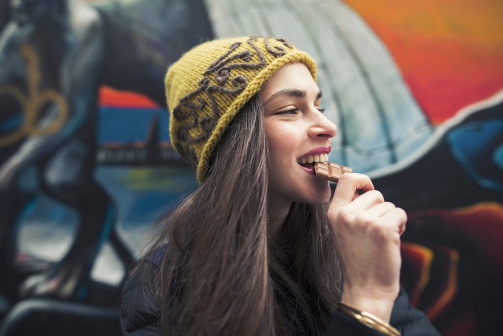 A young woman in a beanie hat eating a slab of vegan chocolate