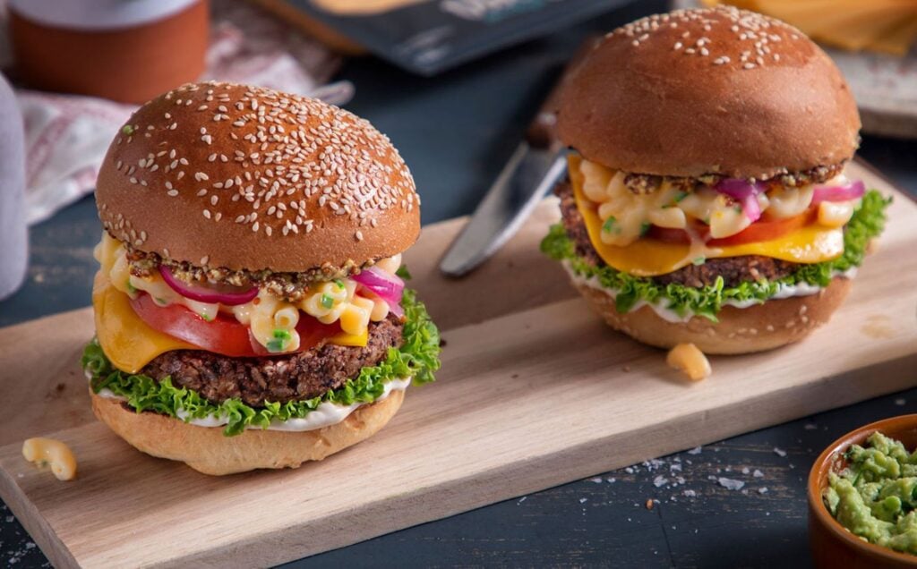 Two fully loaded vegan bean burgers topped with dairy-free mac and cheese and served in bread buns