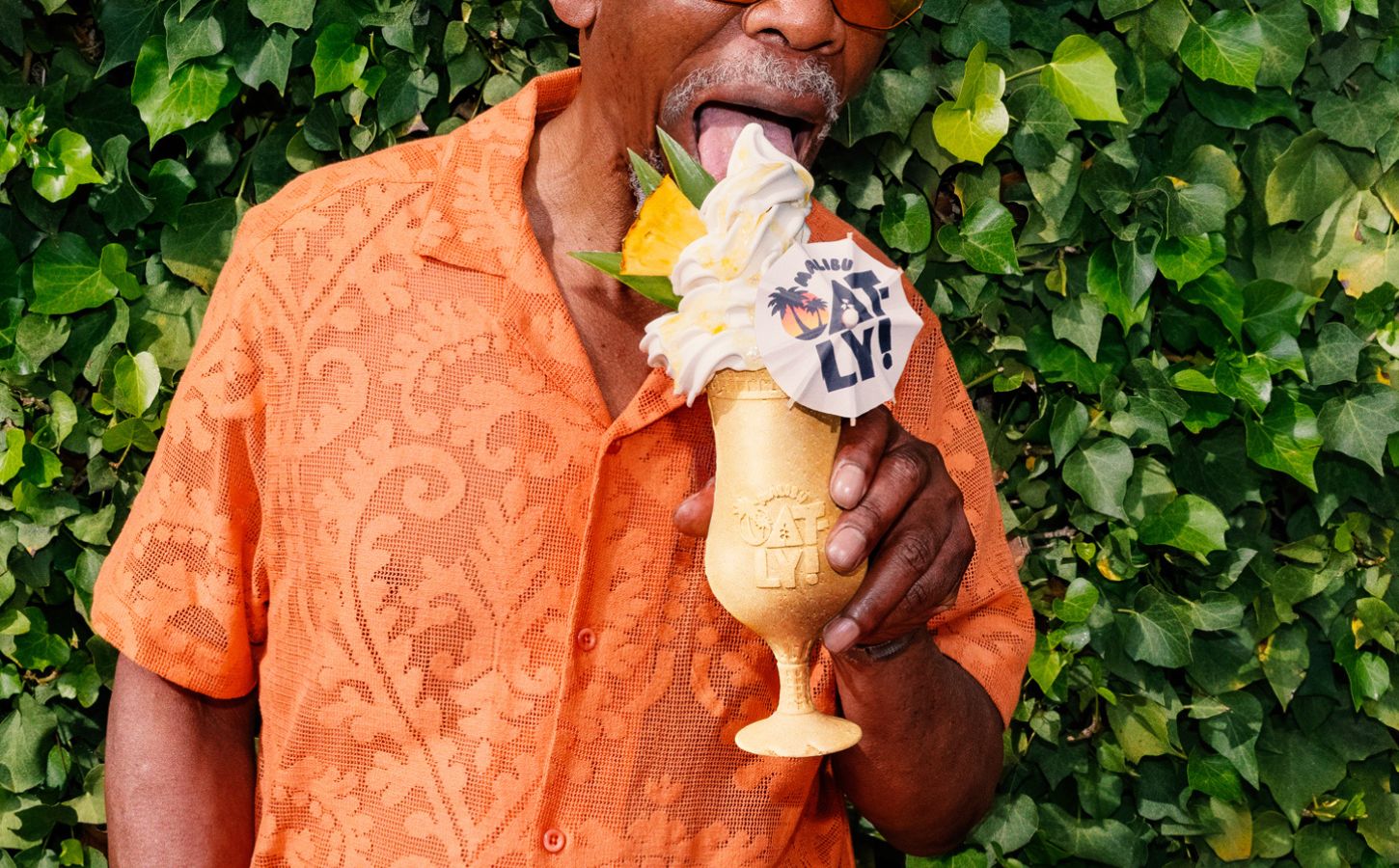 Photo shows a middle-aged Black man in a summery orange shirt holding Oatly and Malibu's new cocktail-inspired alcoholic soft serve, the "Piña Oatlada"